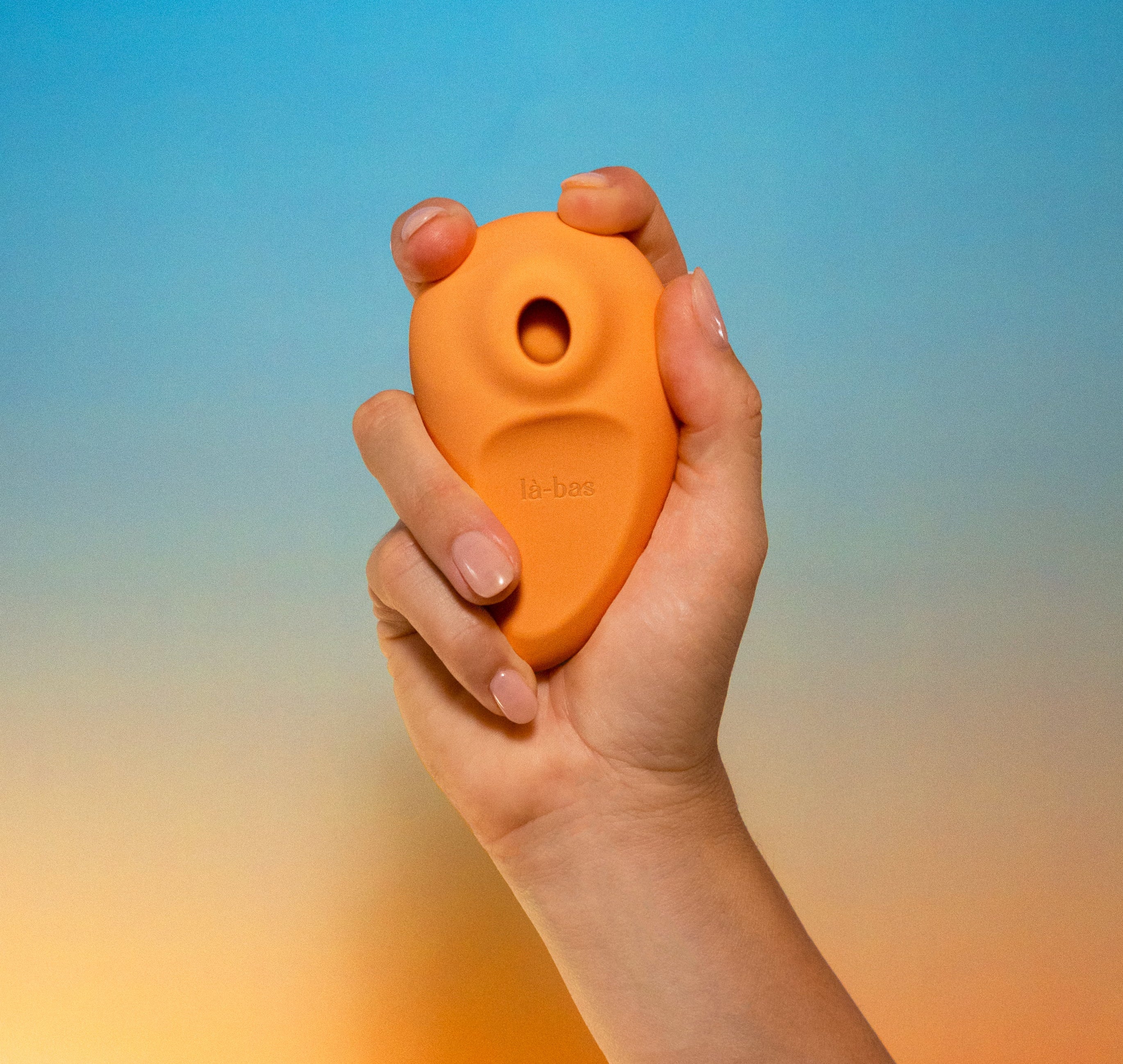 Labas Orae mango/orange-colored pleasure massager held in hand to show its compact, ergonomic shape and soft-touch silicone texture, designed for ocean-deep suction and gentle stimulation.