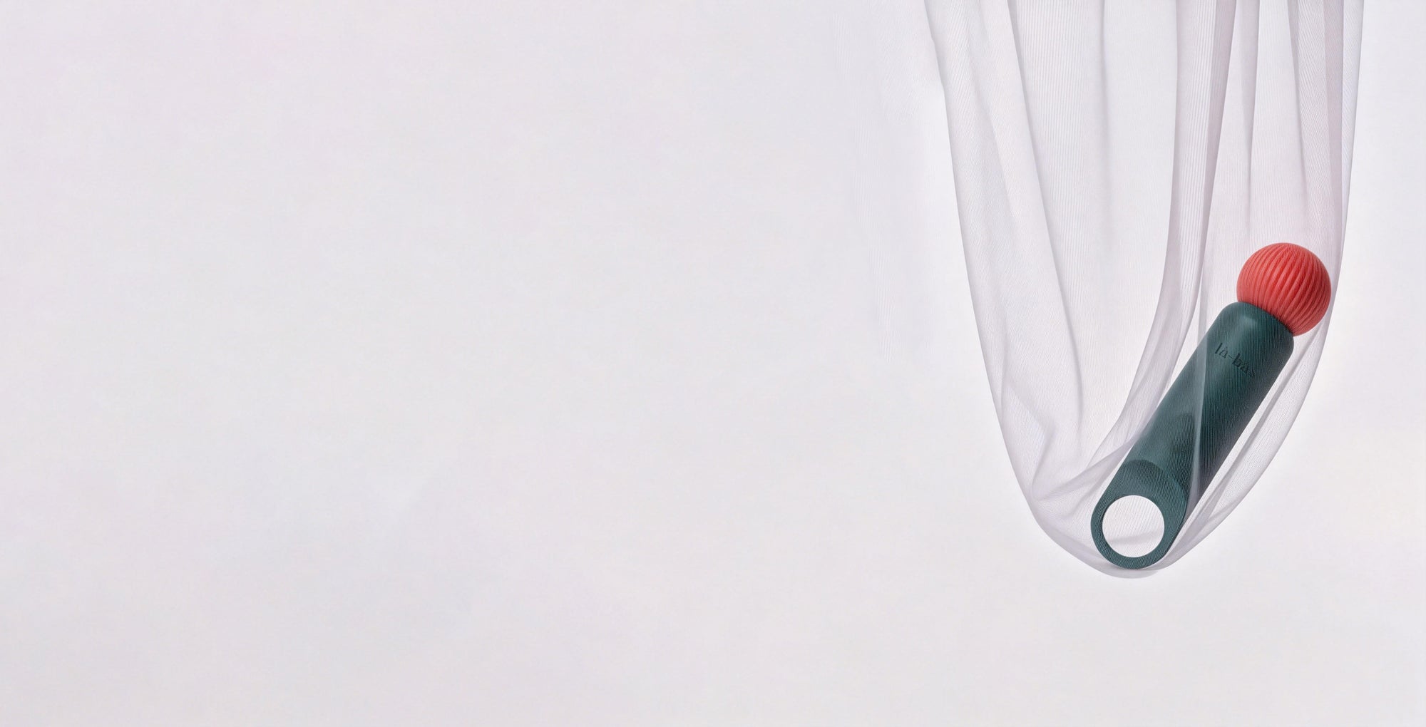 Labas Veya green vibrator resting in a sheer fabric drape, minimalist lifestyle product photography for website background