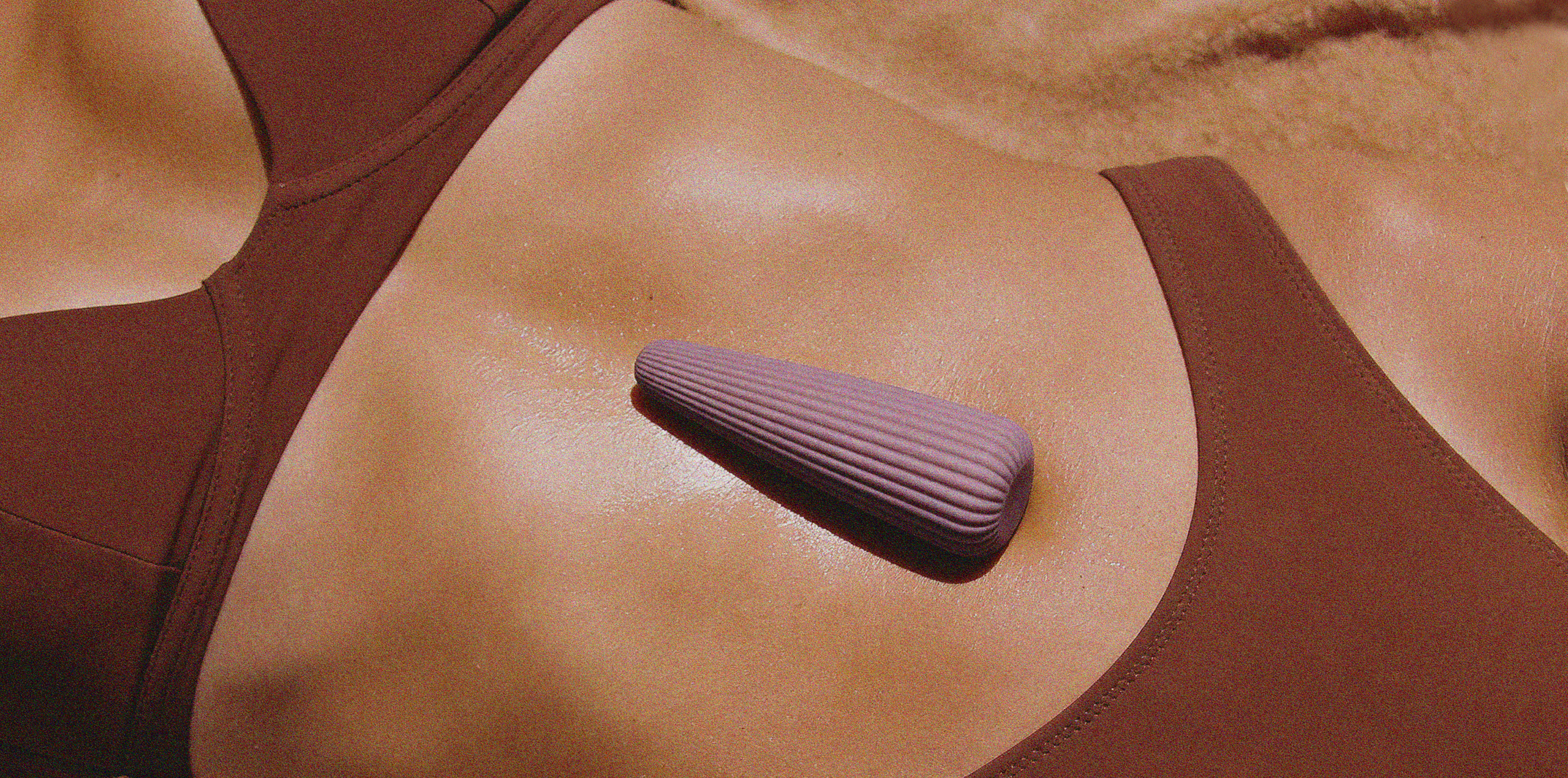 an item laying on the model's belly with shining skin on the beach 