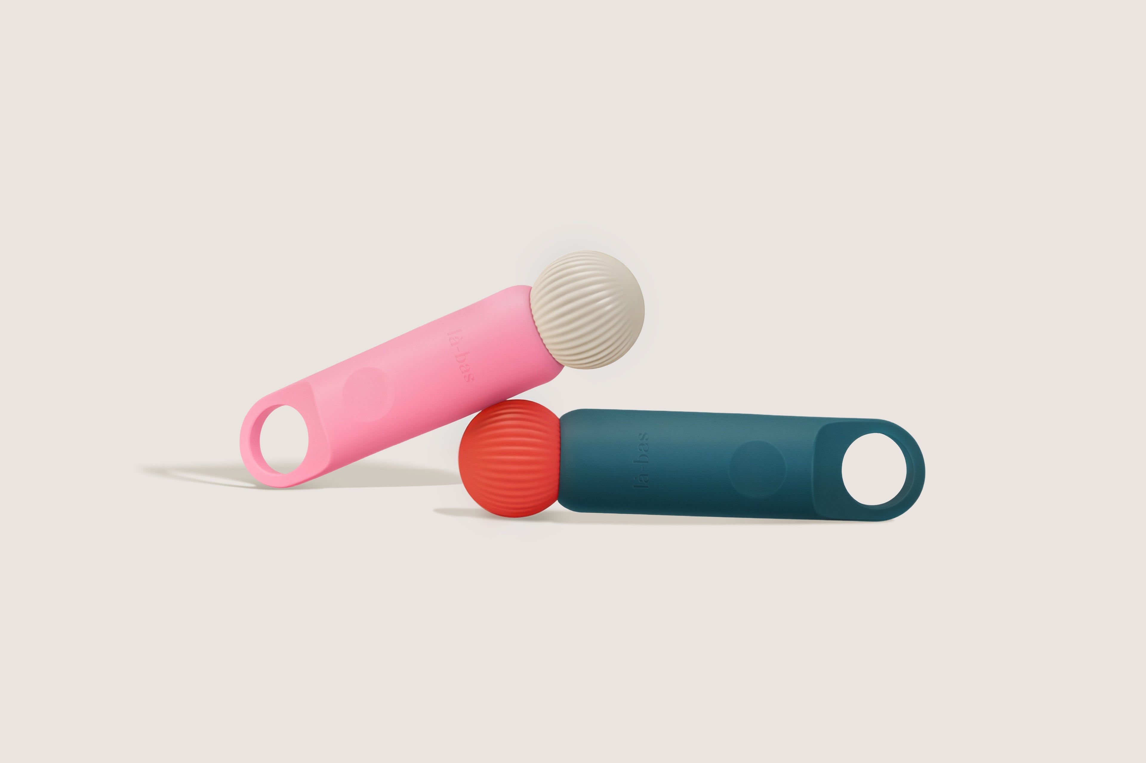 Two La-bas Veya personal massagers/vibrators shown together in pink and teal green colors, featuring a sleek design with textured massage heads.